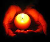 Hands cupping a round glowing candle in prayer.