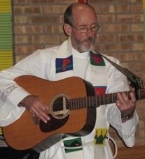 Father Paul T. Brouillette, vested to preach or preside at the altar, playing the guitar